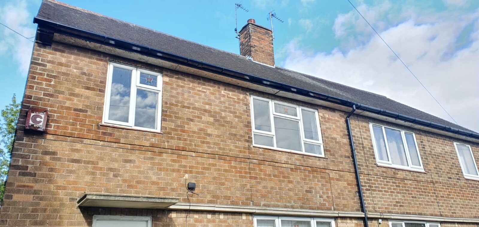 Close view along the eaves of the same house, showing the new black gutter and downpipe against the brickwork