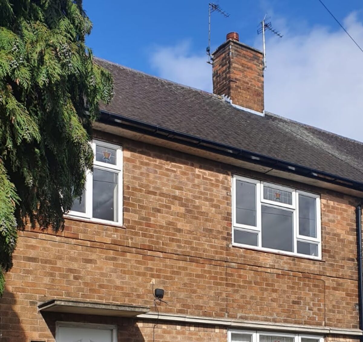 Front elevation of a red brick semi with a new black gutter run along the eaves and a downpipe at the corner